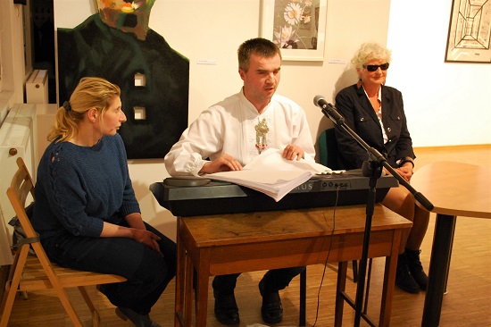 Niewidomy mężczyzna przygotowuje się do gry na keyboardzie i prezentuje śpiewnik zapisany Braillem. Po jego obu stronach siedzą niewidome kobiety.