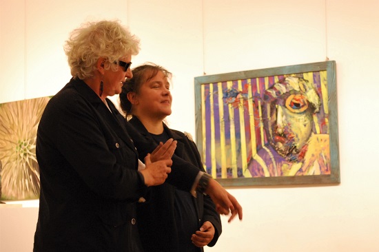 Niewidoma kobieta prowadzi widzącą kobietę, ktora ma zamknięte oczy.